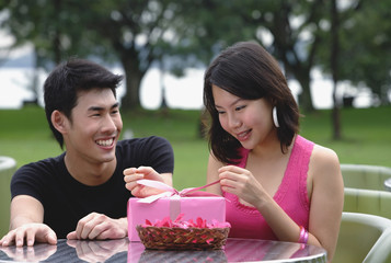 Woman unwrapping a gift, man crouching next to her, smiling