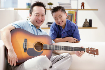 Father and son smiling at camera, father holding guitar