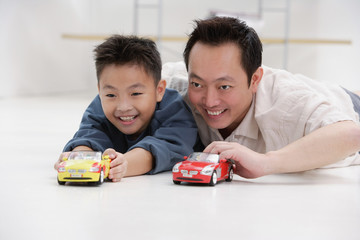 Father and son lying on floor, playing with toy cars