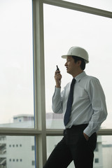 man wearing hard hat, talking into walkie talkie and looking out window