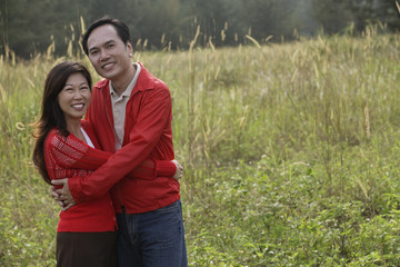 Man and woman hugging each other, standing outdoors in nature, smiling