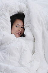 Young woman covered by blanket, smiling at camera