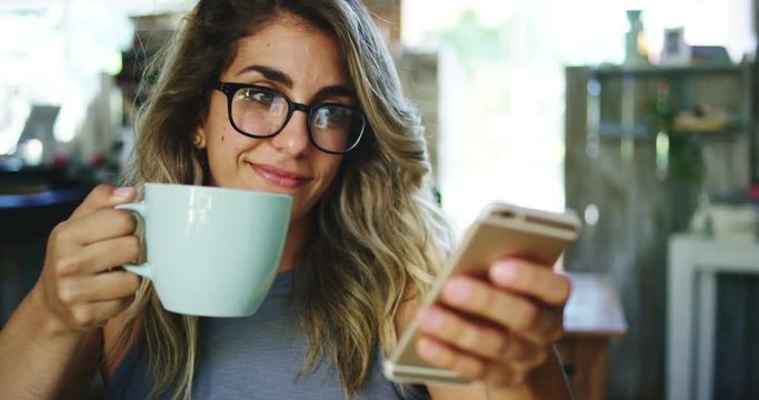 Woman using smartphone while drinking coffee in a cafe