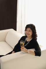 Naklejka premium elegant woman sitting on couch with glass of champagne