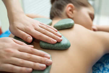 Massage therapist puts spa stones on girl's back