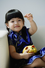 A small girl in blue silk cheongsam plays with a piggy bank