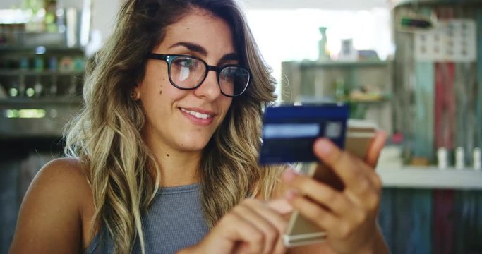 Woman using credit card shopping online with smartphone in cafe
