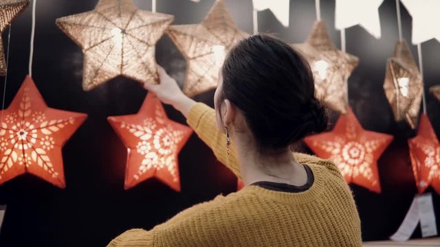 Young attractive brunette girl at the store chooses lamps Star Lights, Christmas decor.