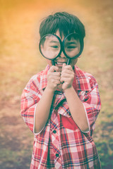 Asian child with magnifying glass at park on vacation. Education