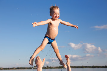 Obraz premium male hands tossing up the kid in the water. fun in the water. father throws the little boy up high. the concept of family lifestyle, summer vacation.