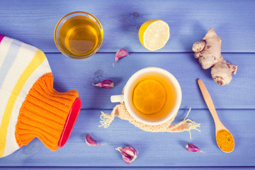 Hot water bottle, cup of tea and ingredients for preparation warming beverage