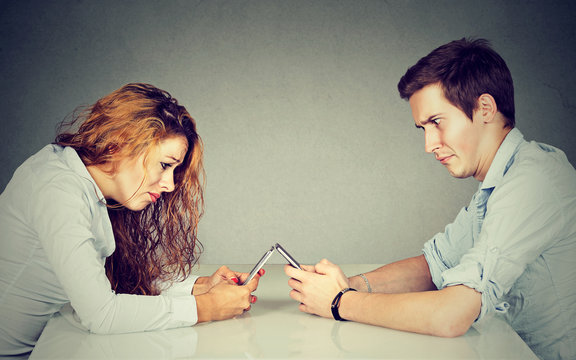 Frustrated annoyed young woman and man sitting at table with smartphone