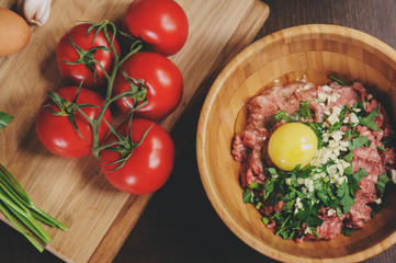 Obraz na płótnie Canvas Raw minced meat with egg, herbs and fresh tomatoes on wooden table. Ingredients for cooking meat balls or loaf in rustic kitchen