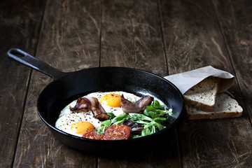 Breakfast set. Pan of fried eggs with bacon, tomato on wooden background