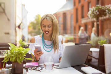 Woman sitting in cafe with laptop and chatting on her mobile phone