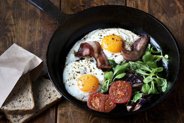 Breakfast set. Pan of fried eggs with bacon, tomato on wooden background