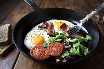 Breakfast set. Pan of fried eggs with bacon, tomato on wooden background