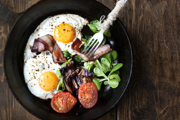 Breakfast set. Pan of fried eggs with bacon, tomato on wooden background