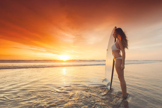 Surfer girl on beach at sunset