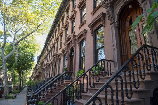 Leafy summer view of the row of stoops on one of the iconic streets of the neighborhood of Brownstone Brooklyn in New York City