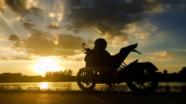 Silhouette motorbike beside the natural lake and beautiful sunset sky.