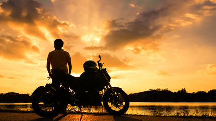 Fototapeta premium Sylwetka rowerzysta z jego motocyklem obok naturalnego jeziora i piękne niebo zmierzchu.
