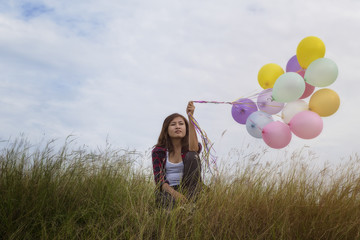 Beautiful girl sitting holding balloons in the prairie grass. On