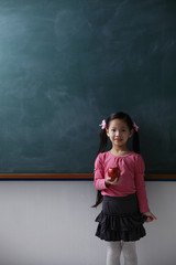 Young girl holding red apple in front of chalk board
