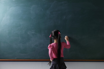 rear view of young girl writing on chalkboard