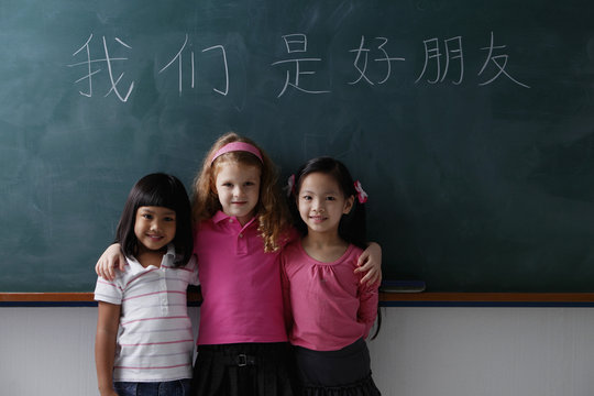 three young girls in front of chalk boards with Chinese writing "we are all friends."
