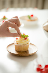 Close up of female hand decorating a cupcake with refreshing mint leaf or picking it. Pastry chef woman making sweet dessert cake
