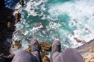 Man in trekking shoes sitting on a high cliff above the Atlanticocean coast (point of view) in Alentejo, Portugal