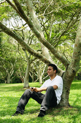 Young man sitting under tree, listening to music