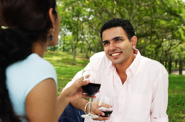 Couple holding wine glasses in park, over the shoulder view