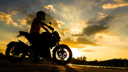 Fototapeta na wymiar Silhouette biker with his motorbike beside the natural lake and beautiful twilight sky.