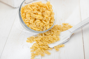 pasta in a transparent plate of glass and wooden spoon on a white old wooden boards