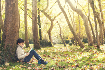 Little boy reading book outdoors