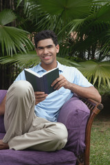 Man with book on chair, smiling at camera