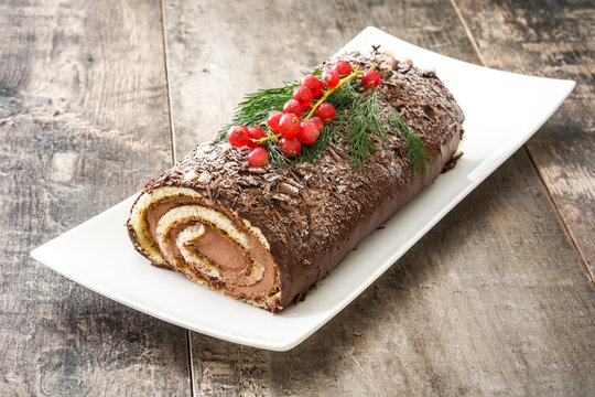 Chocolate yule log christmas cake with red currant on wooden background
