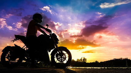 Obraz na płótnie Canvas Silhouette biker with his motorbike beside the natural lake and beautiful twilight sky.