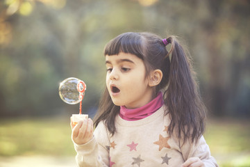 Cute little girl blowing soap bubbles in the park