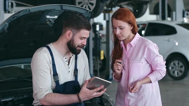 Woman giving her car key to auto service worker after he consulting her about engine repair