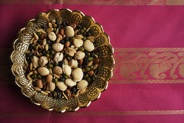 Mix of Indian beans, seeds and nuts in brass dish on pink sari cloth