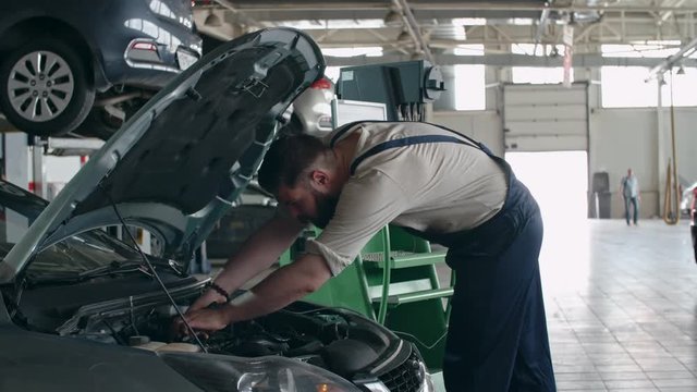 Auto mechanic putting testing tool under the hood of car and using computer to check engine