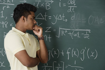 young man standing in front of chalkboard, thinking