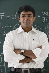 teacher standing in front of chalkboard, arms crossed