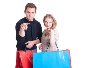 Couple holding shopping bags making watching gesture