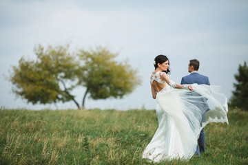 young happy  bride and her husband walking on the meadow