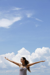 happy young woman raising her arms, blue sky and clouds background.