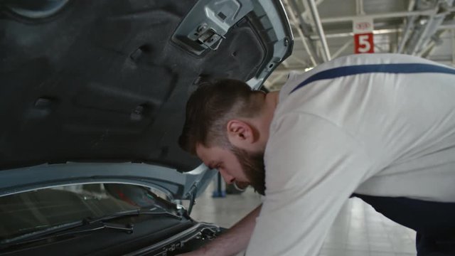 Tilt down of car service worker walking to broken car and using tool to fix something under the hood